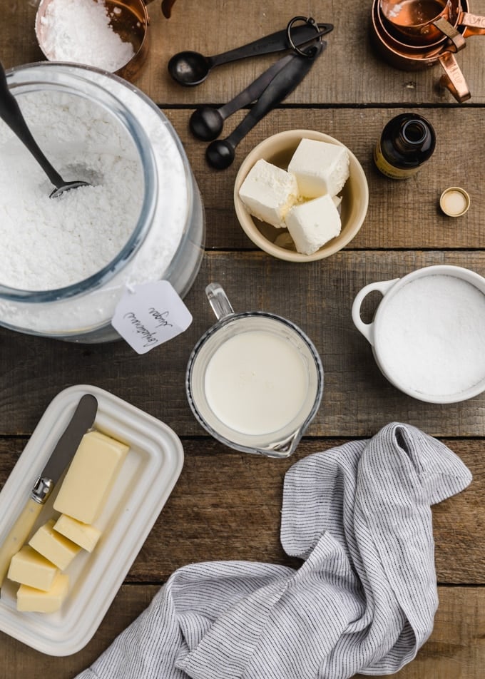 overhead view of ingredients needed for cream cheese glaze on a wood board (butter, confectioner's sugar, cream cheese, milk, salt)