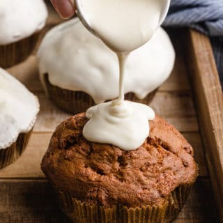 cream cheese glaze being poured onto a cinnamon chip muffin