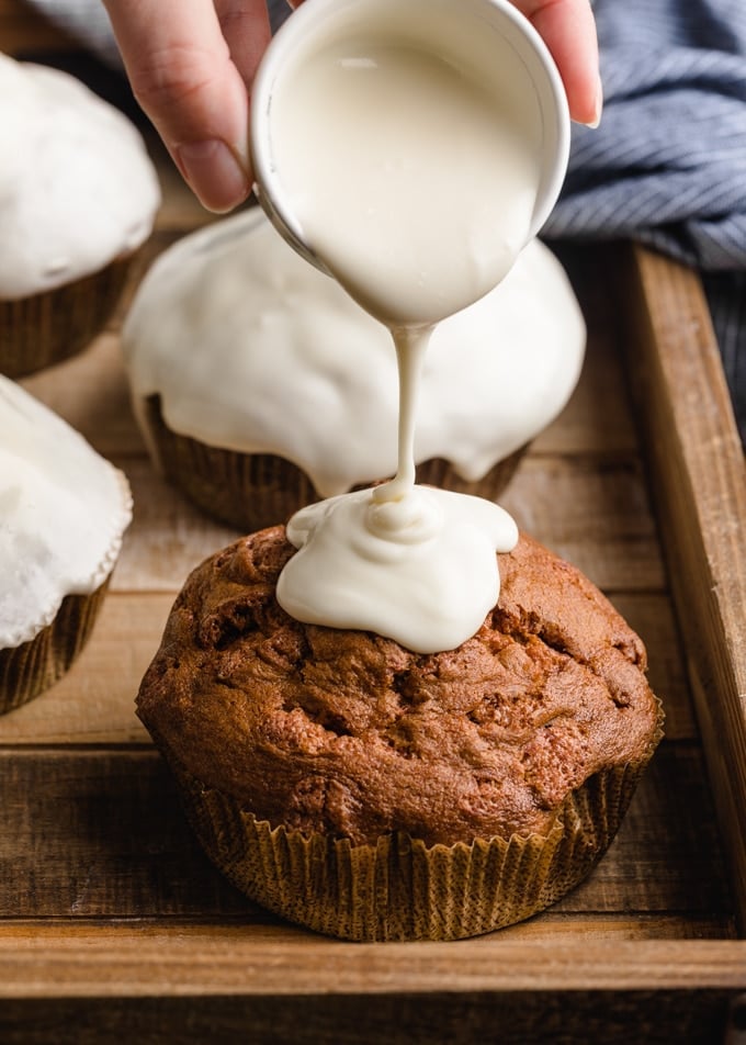 cream cheese glaze being poured onto a cinnamon chip muffin