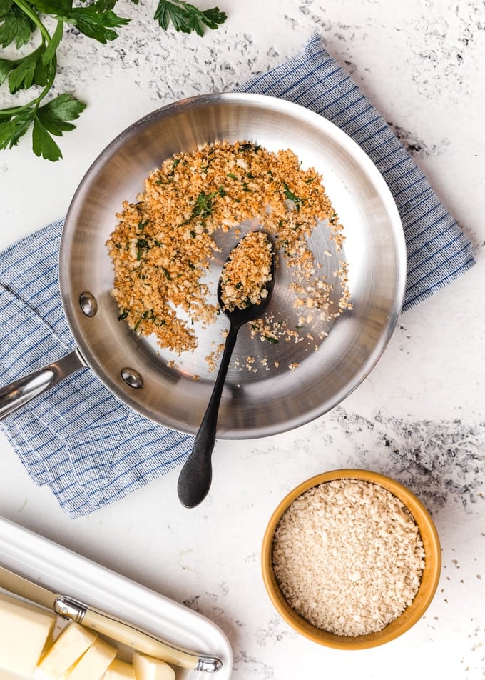 toasted panko breadcrumbs in a skillet, surrounded by butter and a bowl of un-toasted crumbs