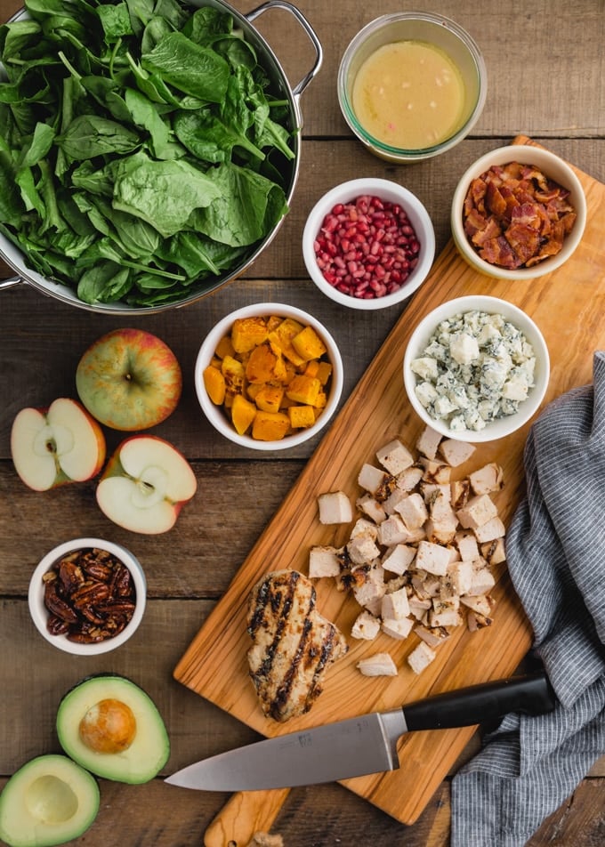 ingredients for harvest cobb salad (apples, chicken, butternut squash, lettuce, blue cheese) on a wood board