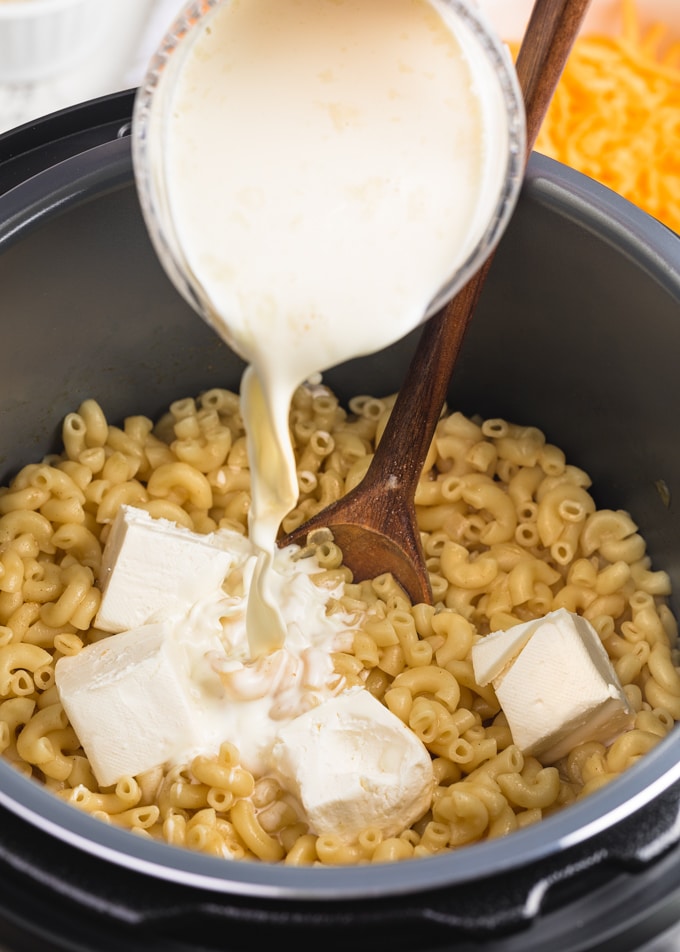 pouring heavy cream into macaroni and cheese in the Instant Pot