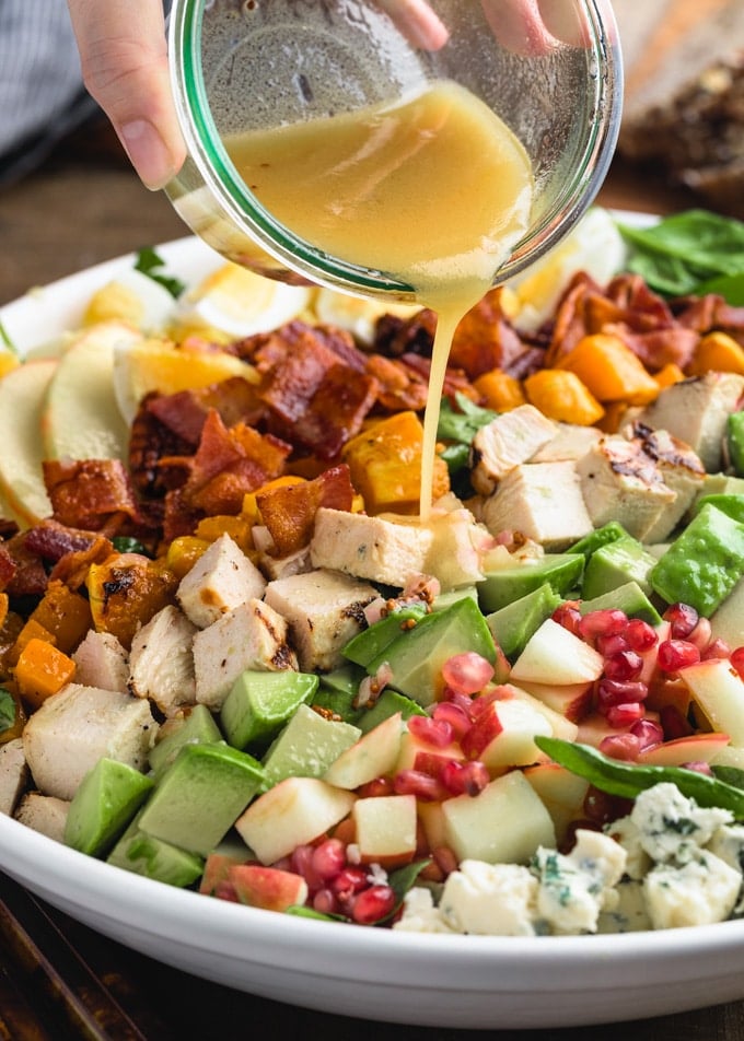 pouring Maple-Dijon Vinaigrette onto a harvest Cobb Salad