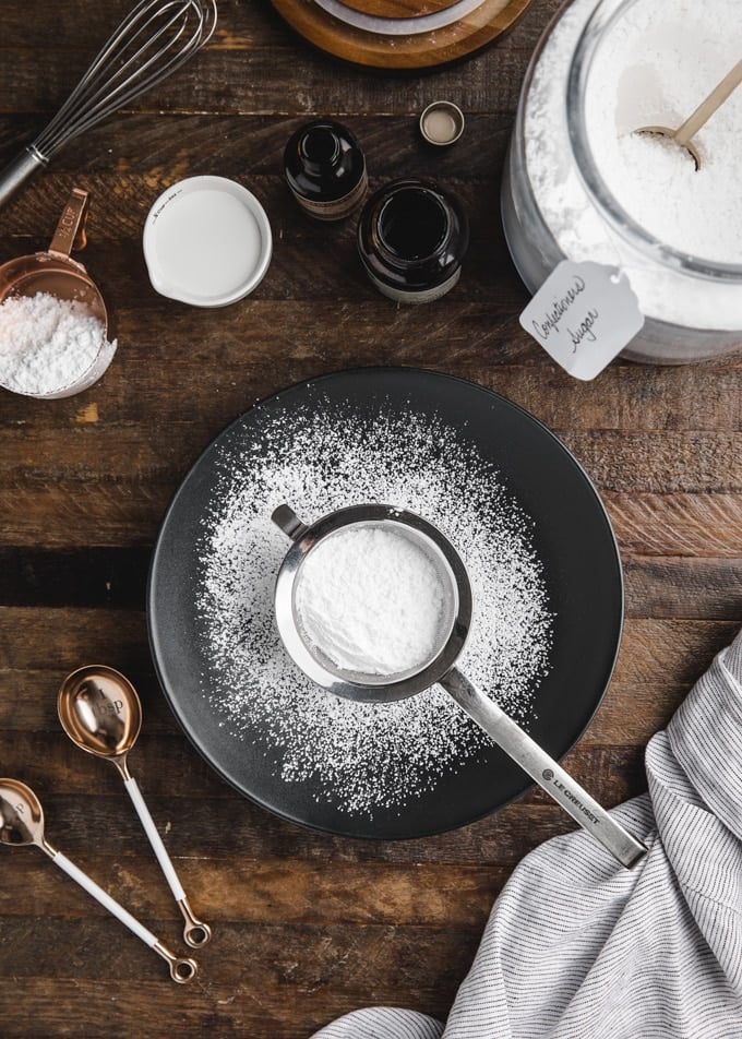 powdered sugar in a sifter sitting in a black bowl on a wood board