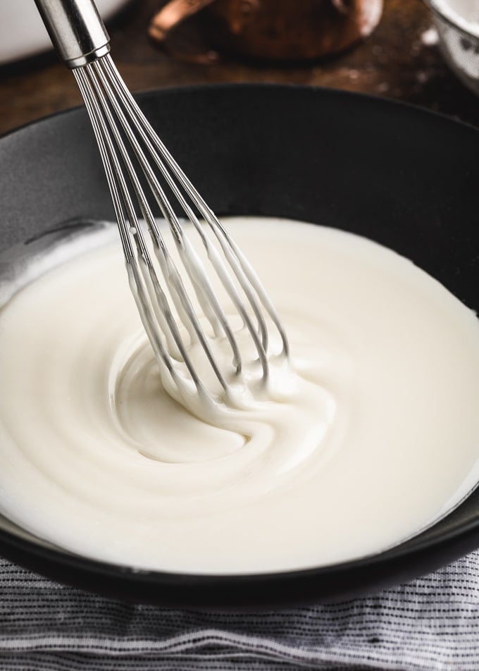 basic powdered sugar cake glaze in a black bowl with a whisk