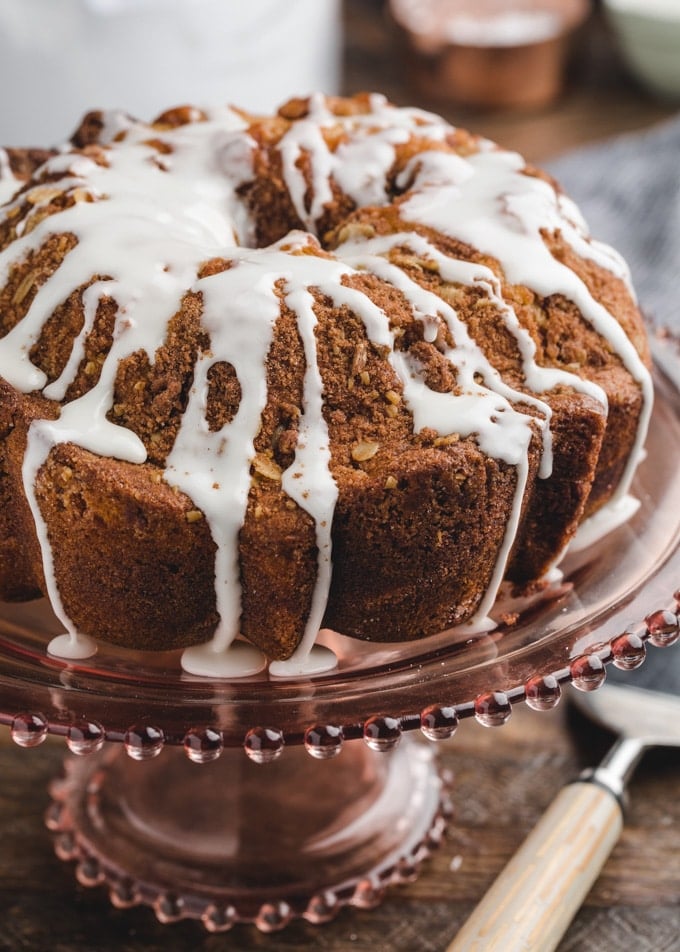 cinnamon coffee cake on a pink glass cake pedestal, drizzled with powdered sugar glaze