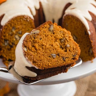 slice of pumpkin bundt cake on a cake server in front of the full cake on a white pedestal