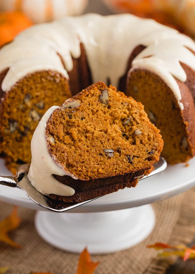 slice of pumpkin bundt cake on a cake server in front of the full cake on a white pedestal