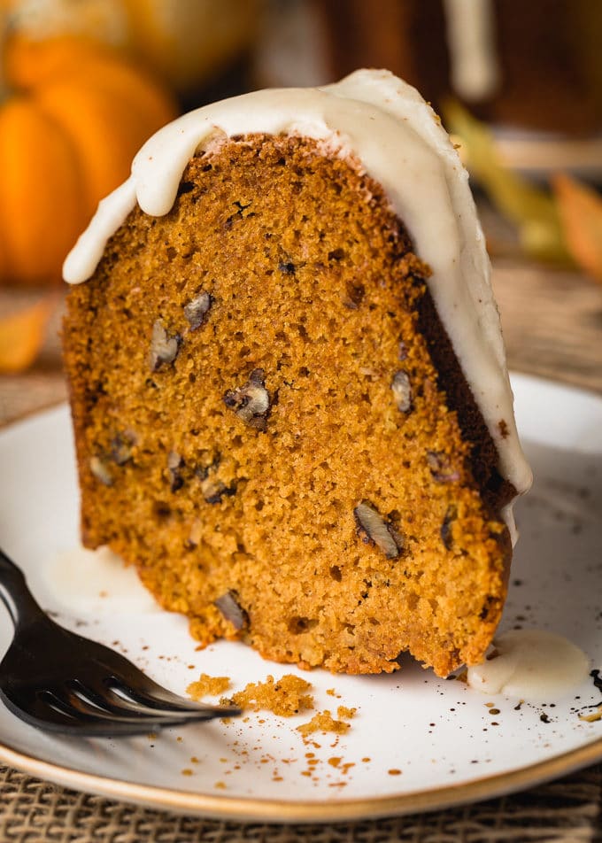 side view of a slice of pumpkin pecan bundt cake on a white plate with a black fork