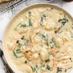 overhead of bowl of rotisserie chicken gnocchi soup on a striped napkin next to a wedge of parmesan cheese