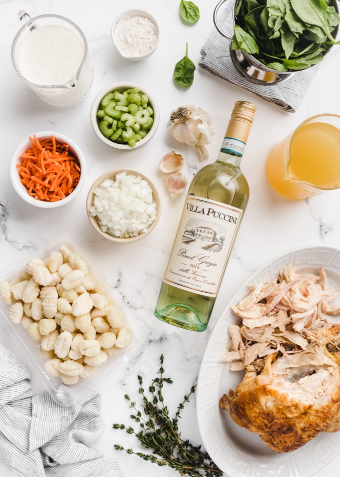 overhead view of ingredients on white marble: gnocchi, chicken, wine, broth, carrots, onions, celery, garlic, half and half, flour, spinach, and stock