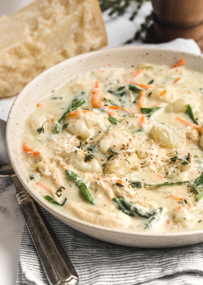 side view of a bowl of rotisserie chicken gnocchi soup, garnished with black pepper and grated parmesan