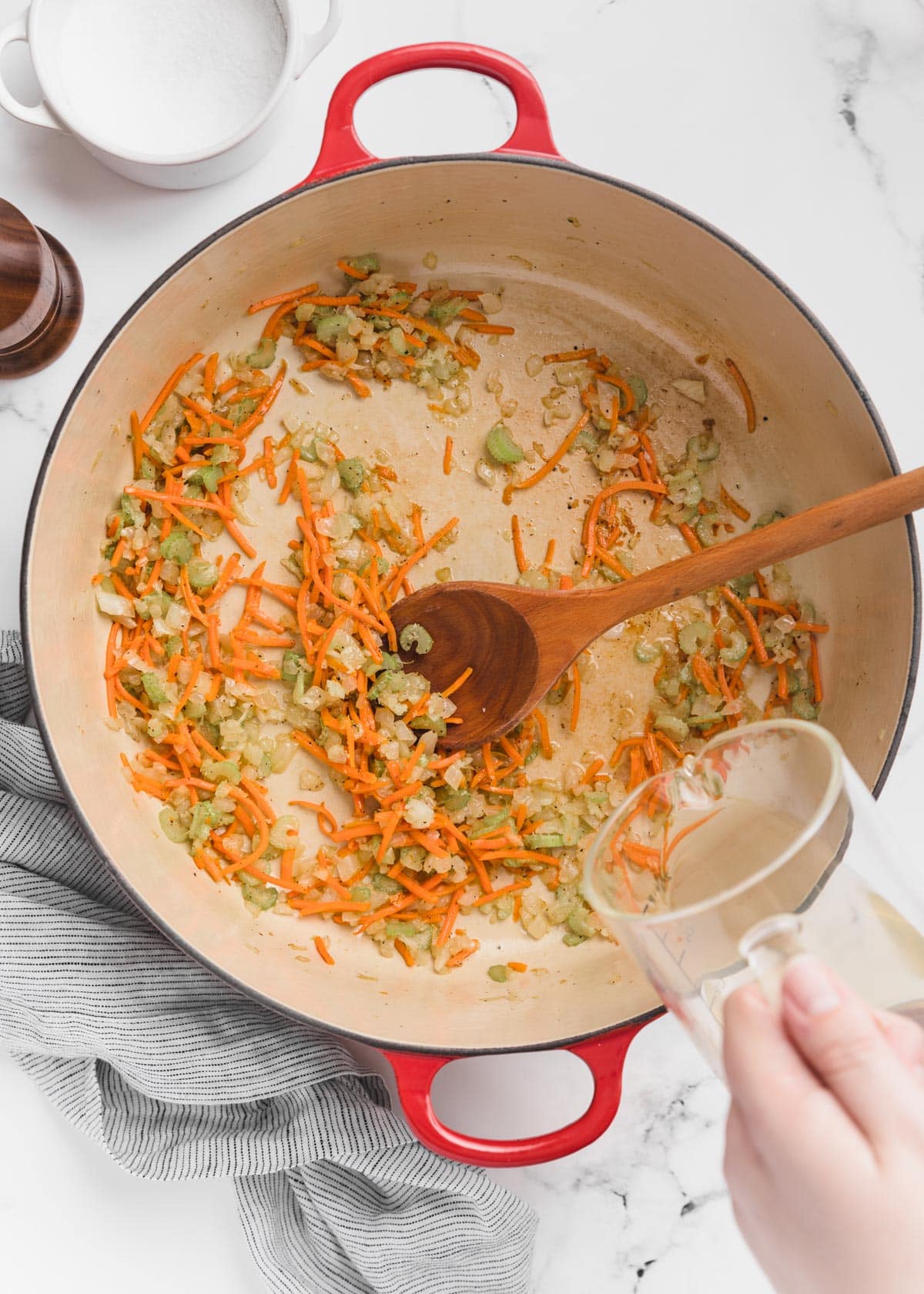 white wine being poured from a glass measuring cup into a Dutch oven with sauteed mirepoix.