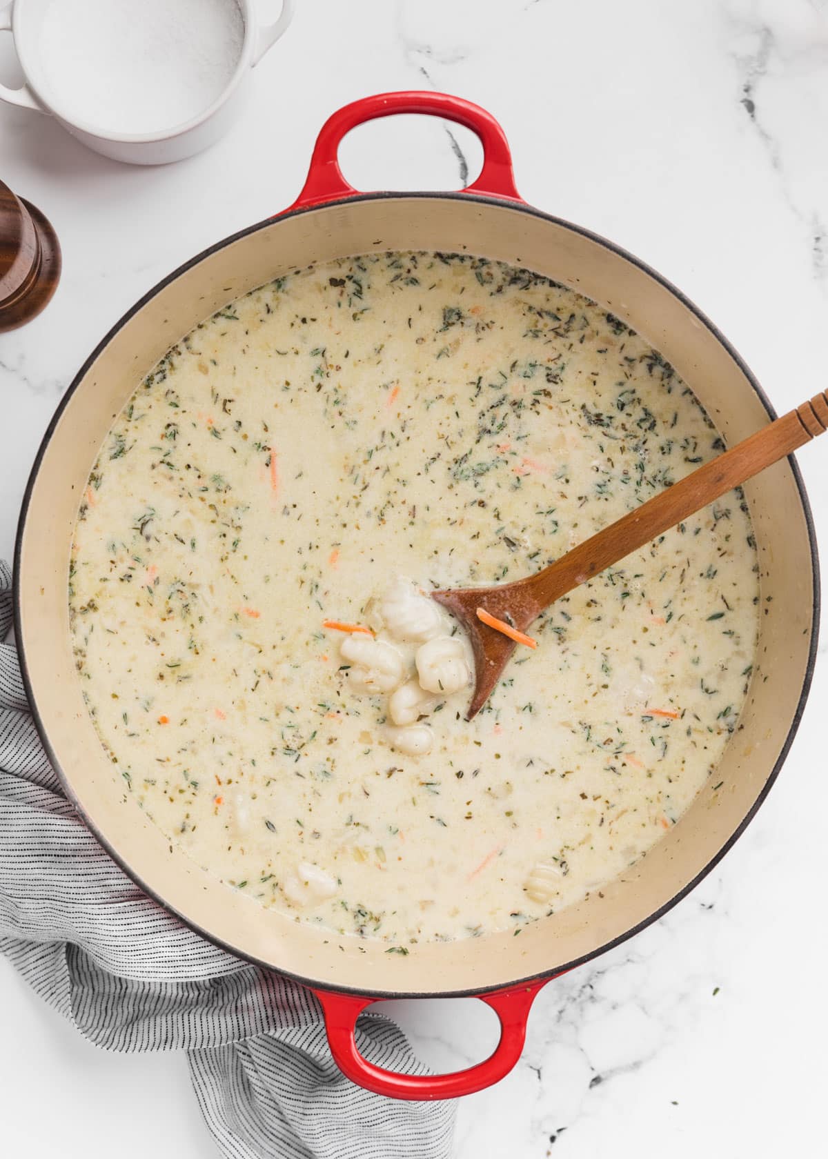 uncooked gnocchi added to soup in a Dutch oven. A wooden spoon sits in the pot.