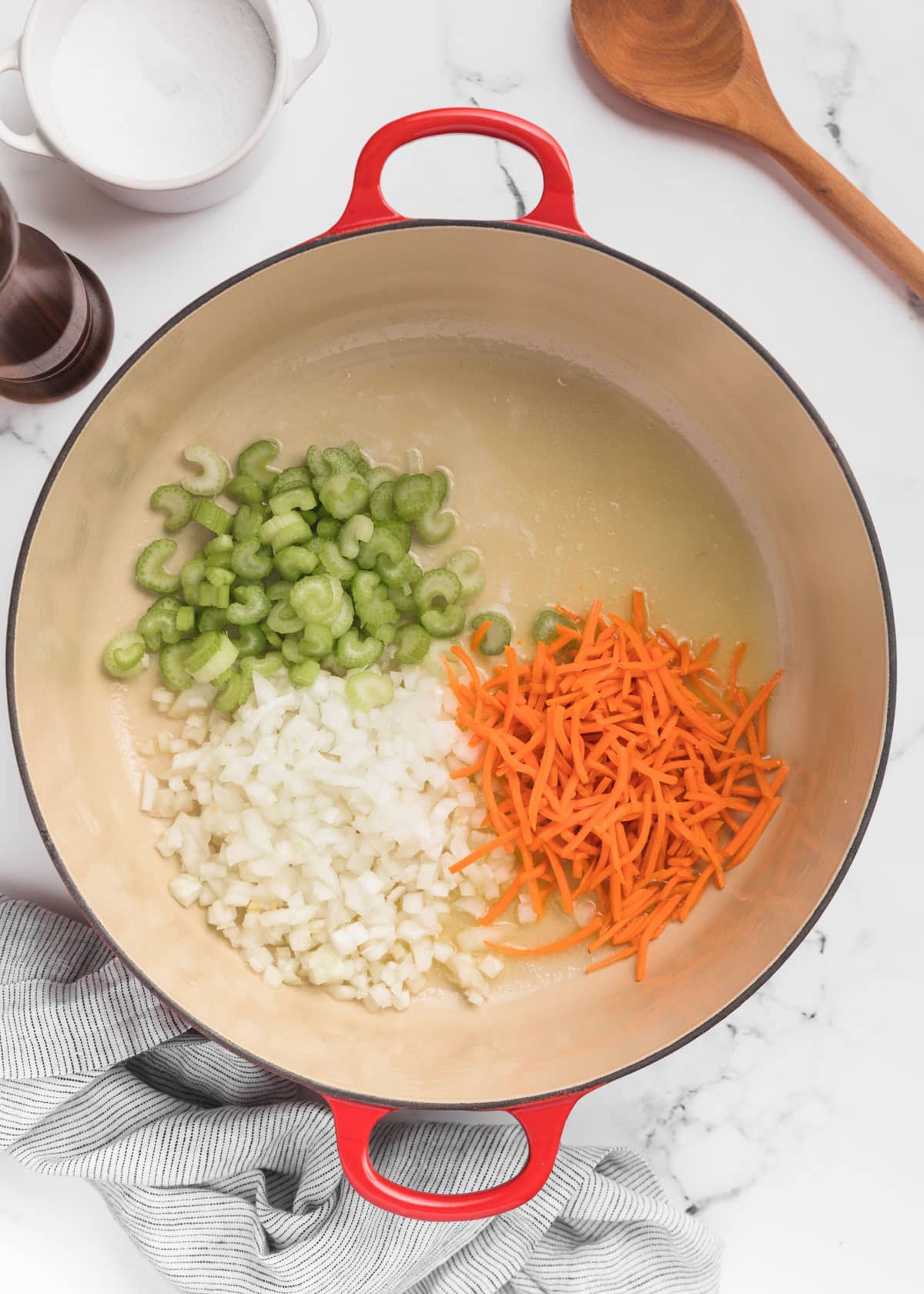 raw carrots, celery, and onions in a Dutch oven on a white marble board