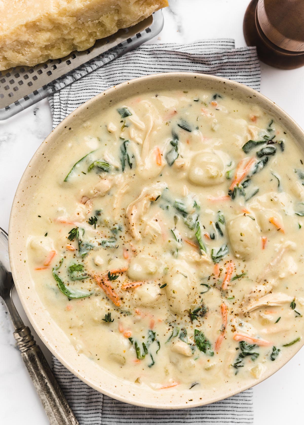 overhead of bowl of creamy rotisserie chicken gnocchi soup on a striped napkin next to a wedge of parmesan cheese