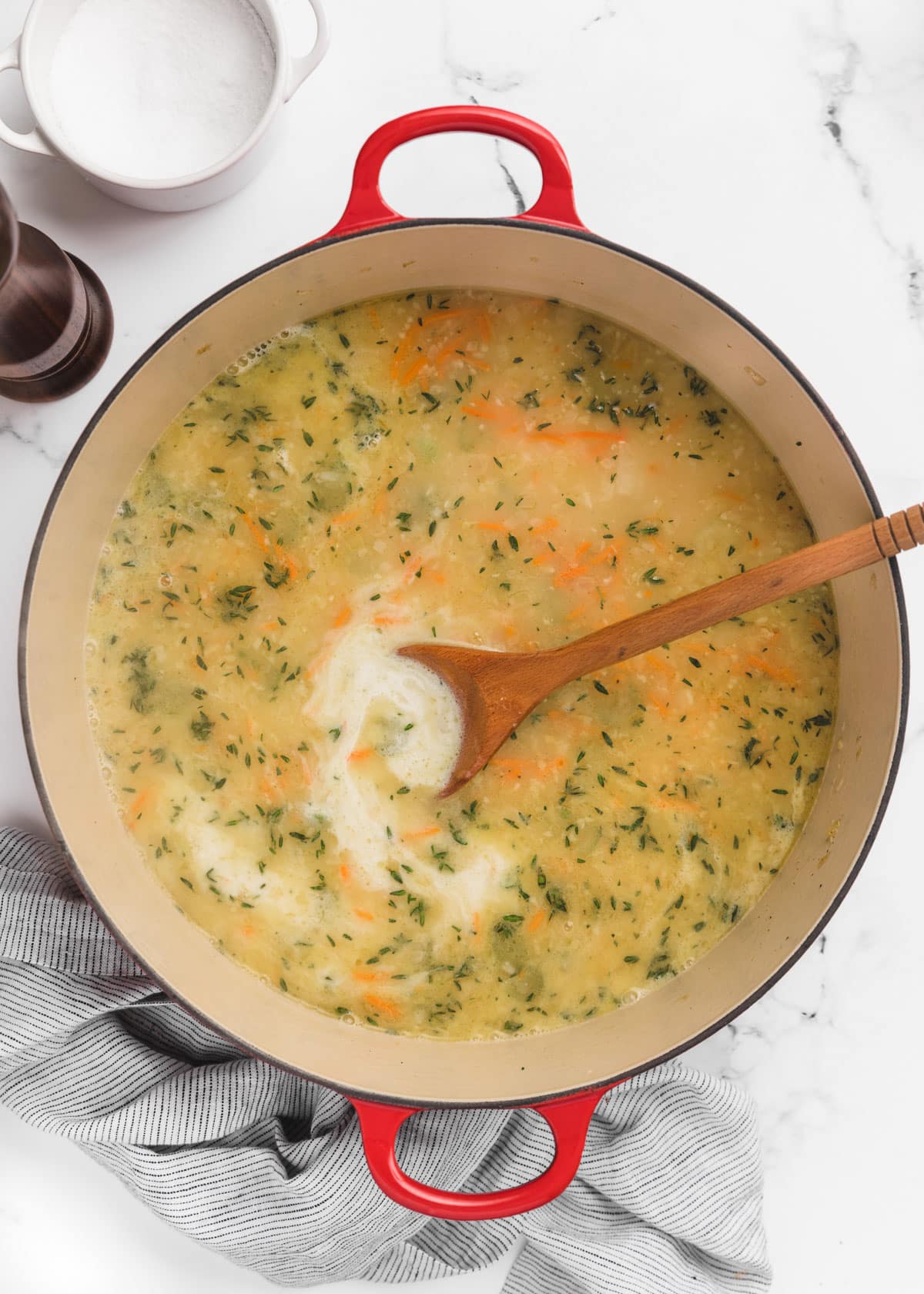 chicken stock, half and half, and herbs added to a Dutch oven. A wooden spoon sits in the pot.