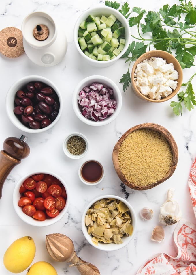 overhead of ingredients for orzo salad 
in bowls on a white marble board