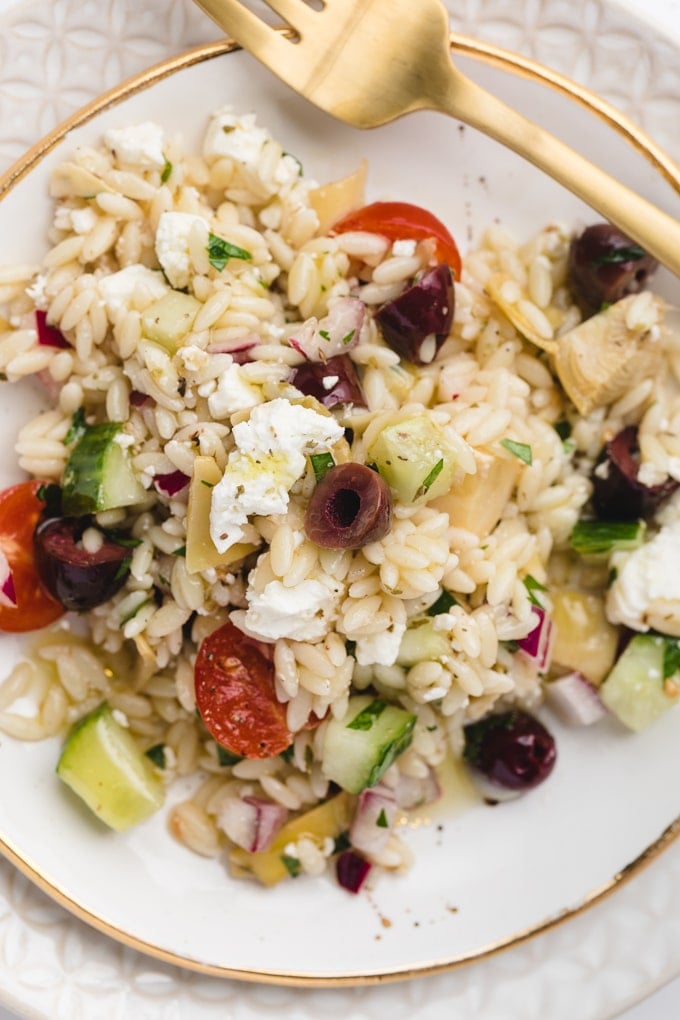 overhead closeup of orzo pasta salad with Feta cheese and kalamata olives on a white and gold plate