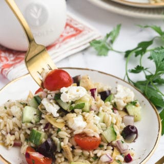 greek orzo salad on a white and gold plate, being scooped up with a gold fork