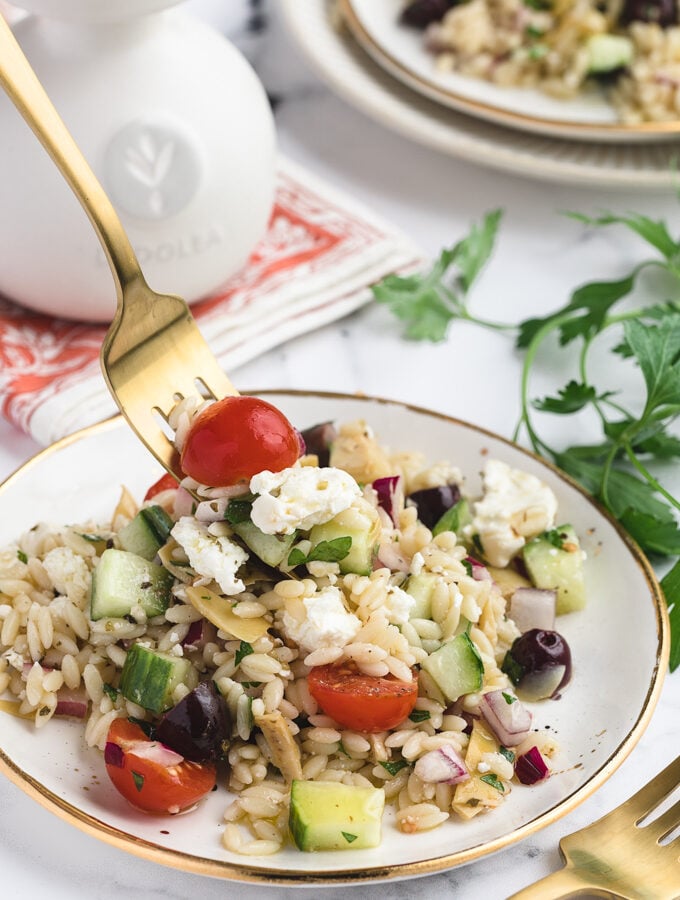 greek orzo salad on a white and gold plate, being scooped up with a gold fork