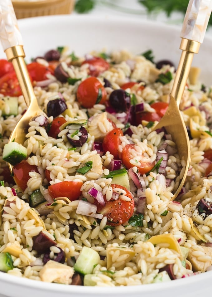 closeup of orzo salad being tossed with a gold salad spoon set