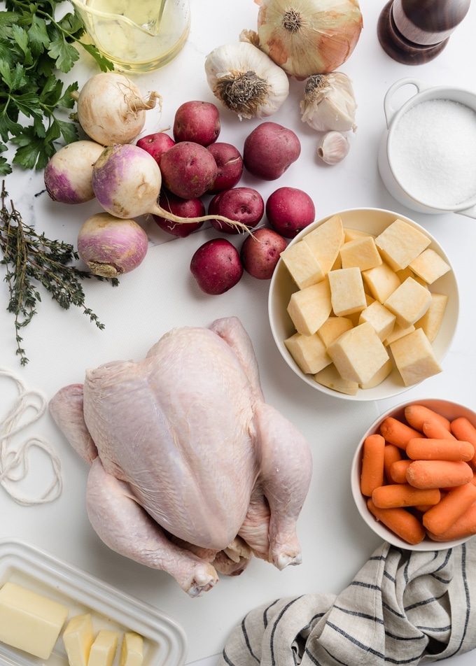 raw whole chicken and root vegetables on a white marble board