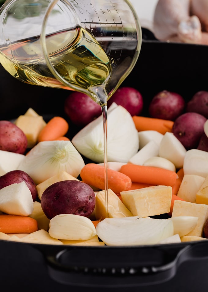 root vegetables in a cast iron roasting pan being drizzled with vegetable oil