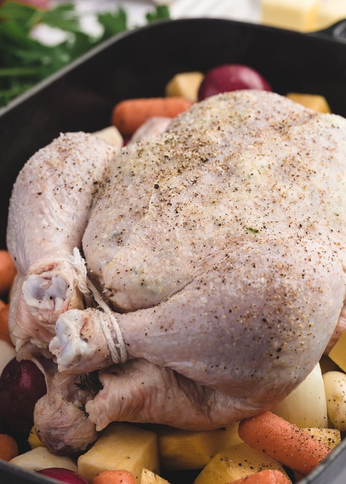 raw whole chicken on a bed of root vegetables in a cast iron roasting pan