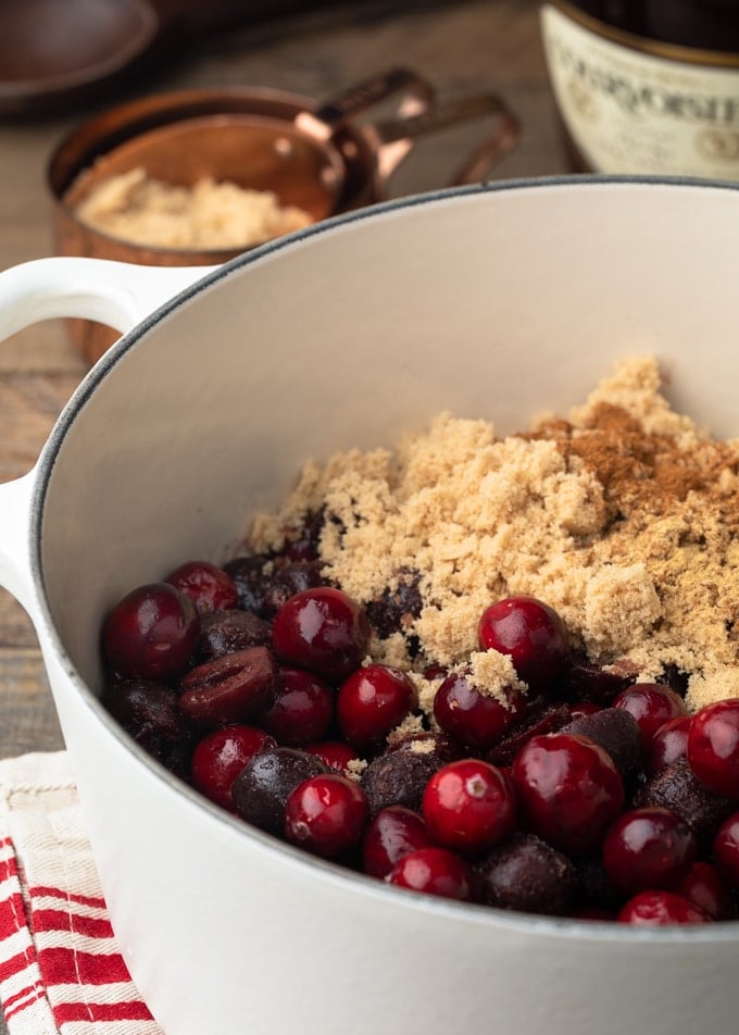 cranberries and frozen cherries in a white pot with brown sugar and cinnamon