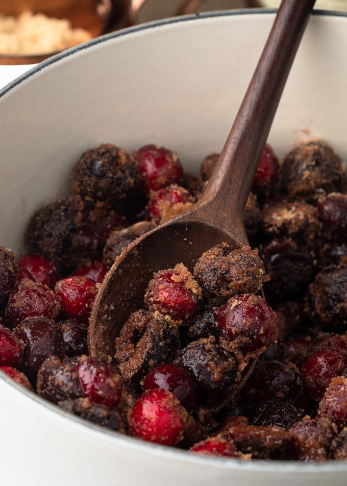 cranberries and cherries tossed with brown sugar and spices on a wood spoon in a white pot 