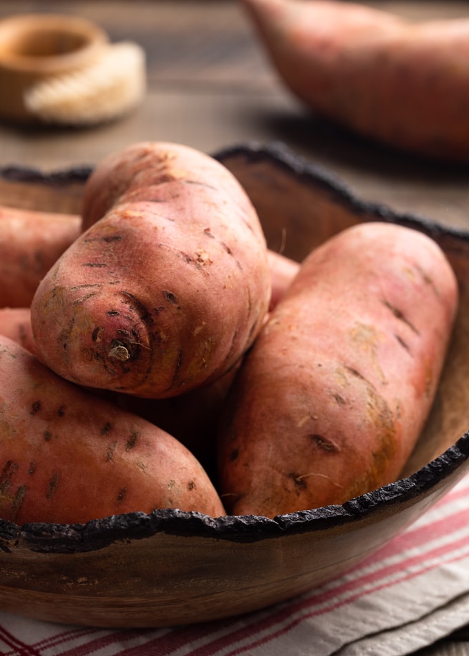 raw sweet potatoes in a large wooden bowl on a beige and red napkin