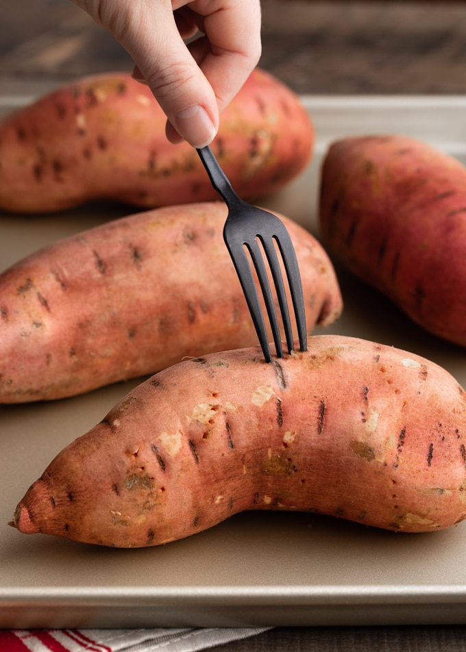 fork piercing raw sweet potatoes on a baking sheet