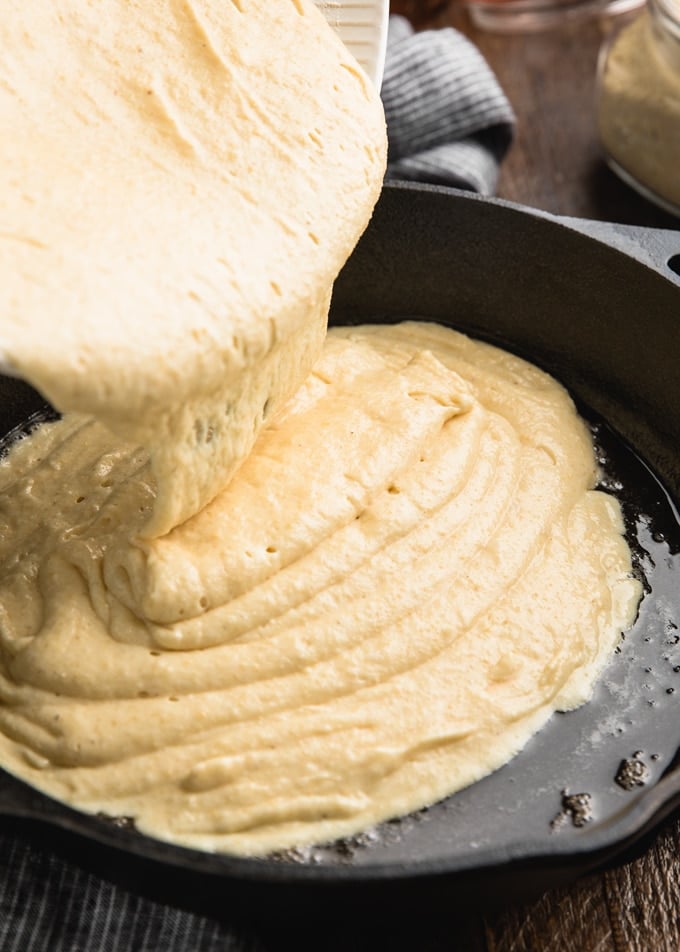 pouring cornbread batter into a hot, buttered cast iron skillet