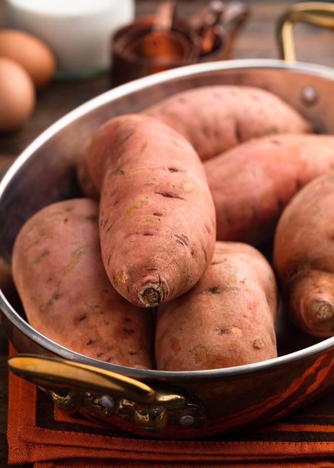 uncooked sweet potatoes piled into a copper baking dish