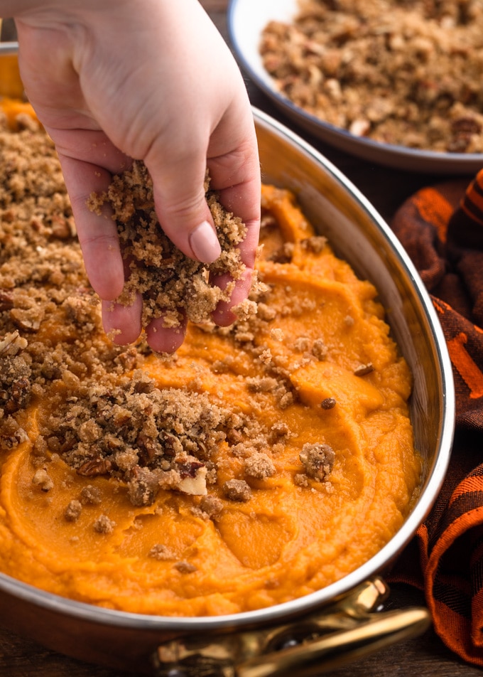 sprinkling pecan streusel topping over an unbaked sweet potato casserole