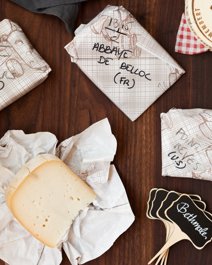 wrapped and unwrapped cheese wedges on a board next to chalkboard tags