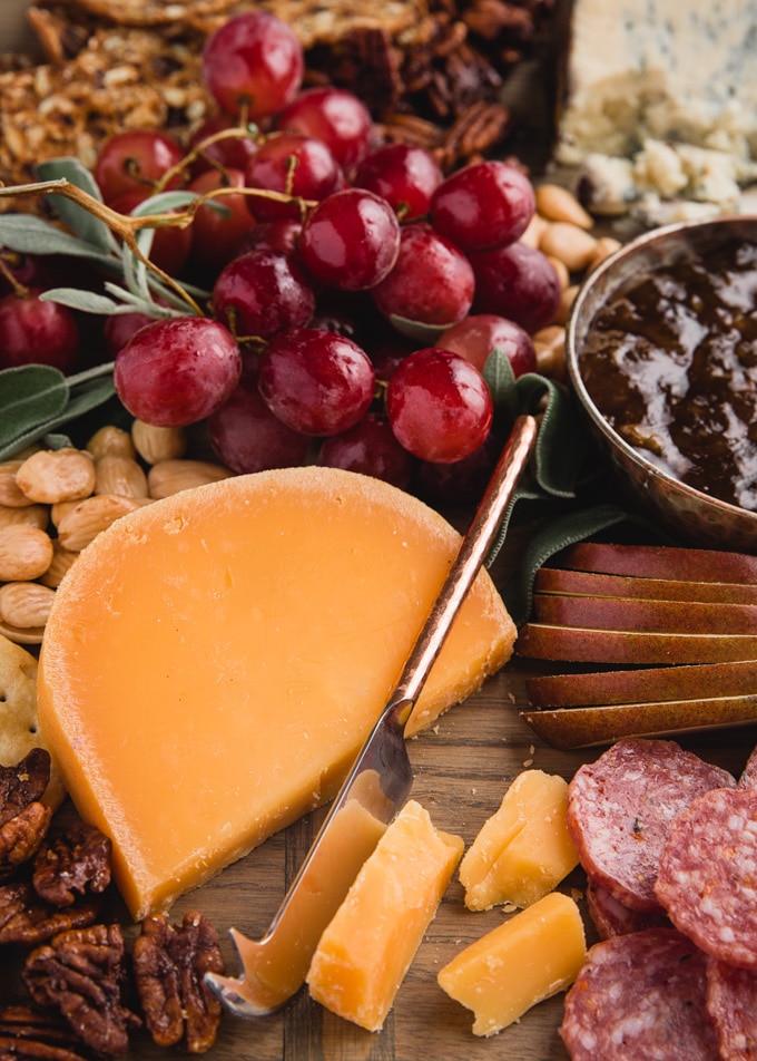 wedge of aged gouda on a cheese board with grapes, pears, charcuterie, and nuts