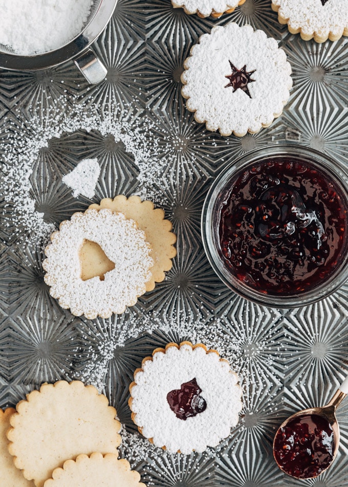 unassembled and assembled linzer cookies on a baking sheet, dusted with powdered sugar