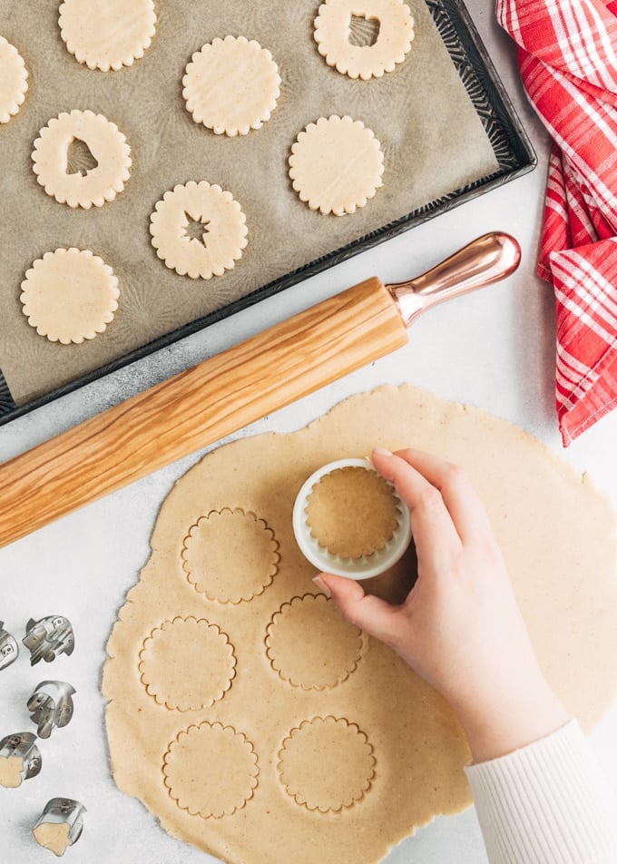 cutting out rounds of linzer cookie dough with a fluted cookie cutter