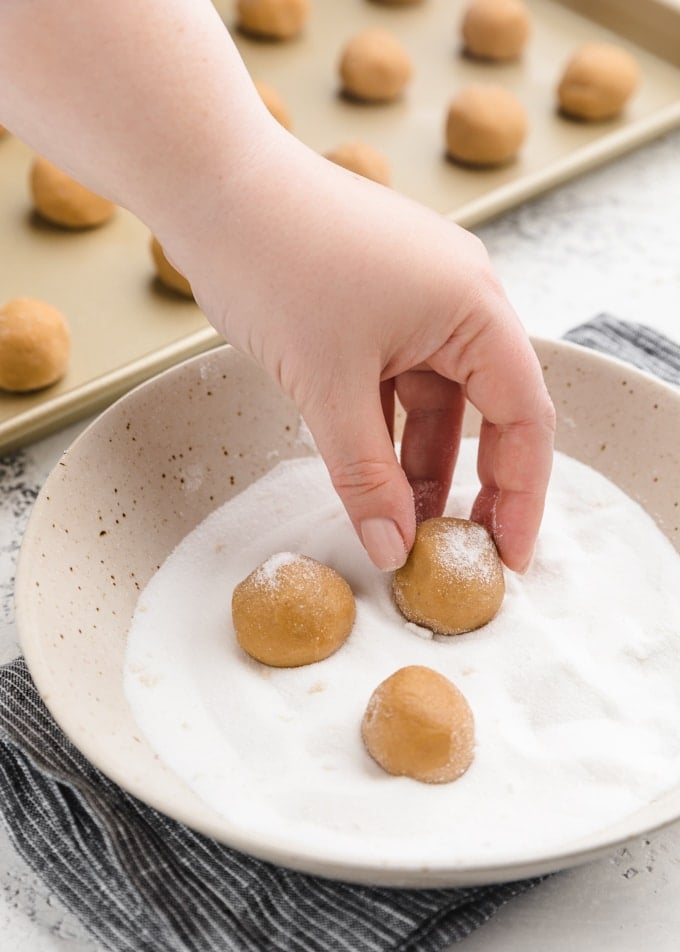 rolling balls of peanut butter cookie dough in granulated sugar in a ceramic bowl