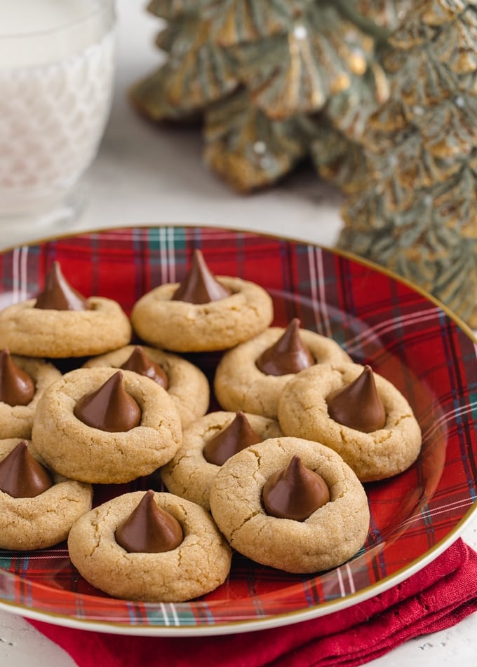 peanut butter blossoms on a red plaid plate with a glass of milk and pine tree-shaped candles in the background