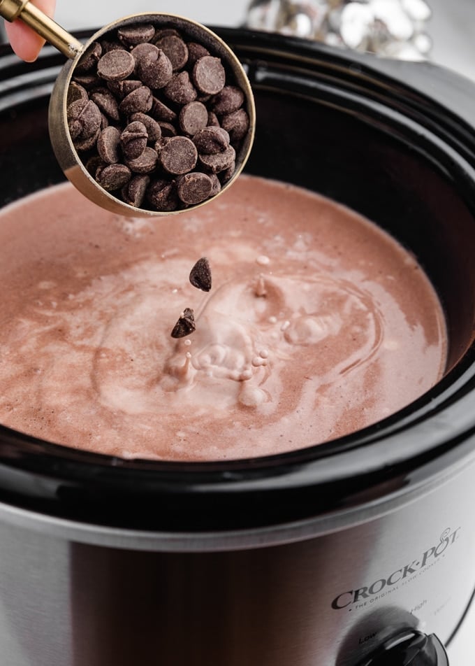 semisweet chocolate chips being poured into a crockpot filled with hot chocolate