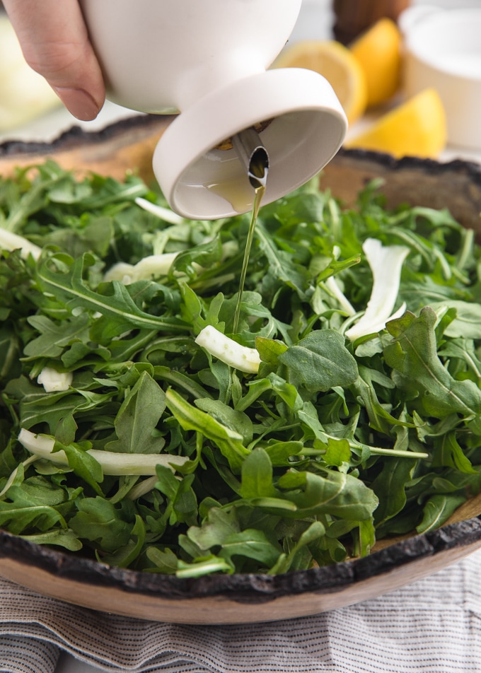 Greek extra virgin olive oil being drizzled over arugula salad in a wood bowl