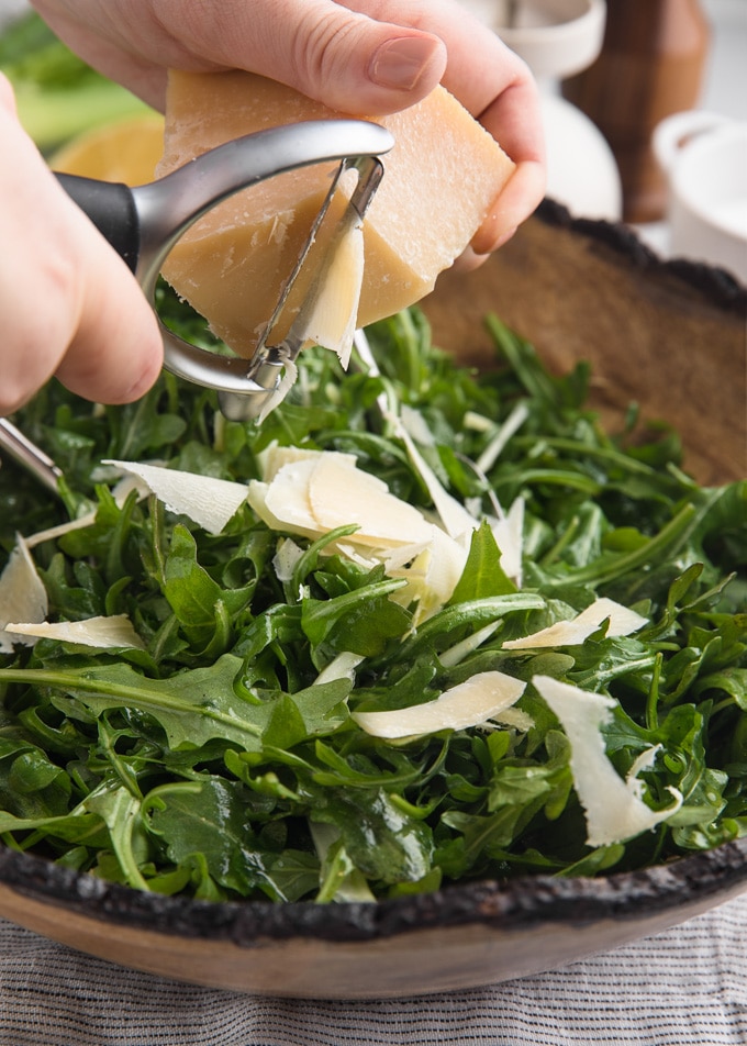 wedge of parmigiano reggiano being shaved over arugula salad