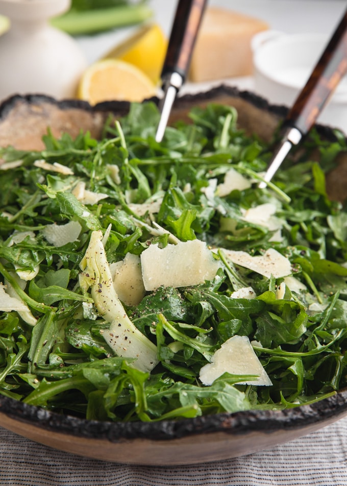 arugula salad with fennel and shaved parmigiano reggiano in a wood bowl with salad servers