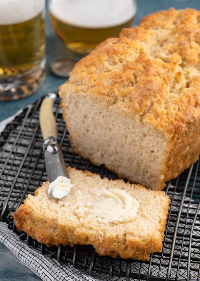 a slice of beer bread next to the baked loaf on a black cooling rack, spread with softened butter