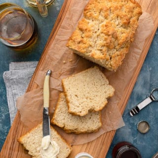 sliced beer bread loaf on a wood serving board with butter and honey