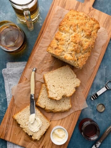sliced beer bread loaf on a wood serving board with butter and honey