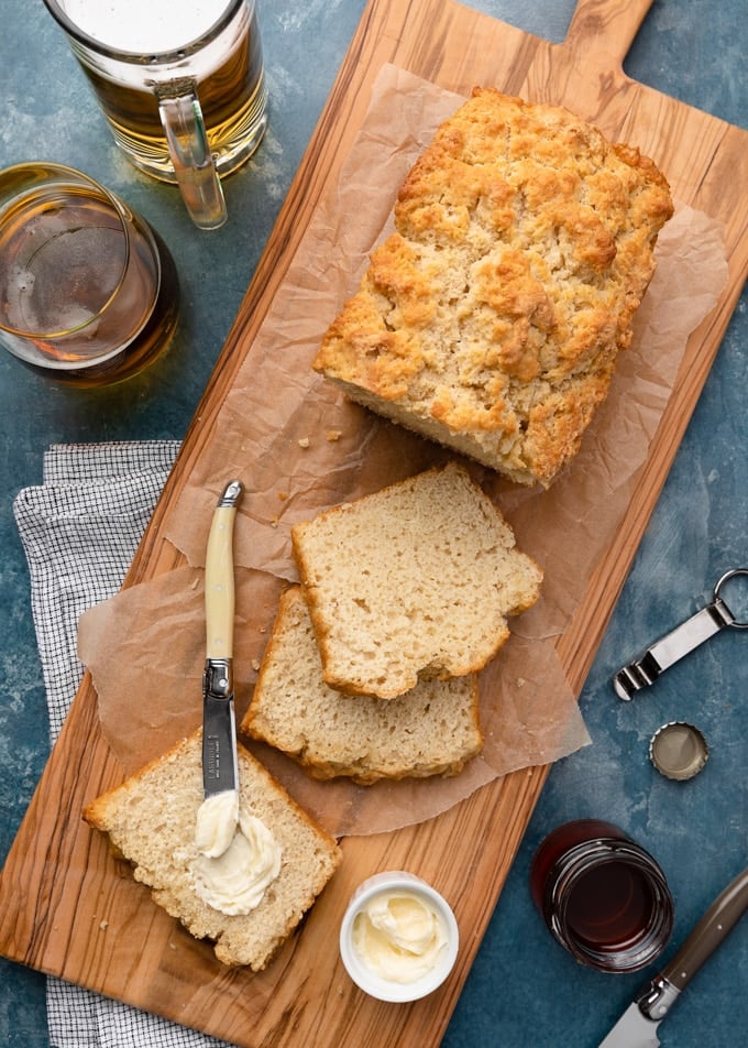 beer bread on a wood serving board with butter and glasses of lager